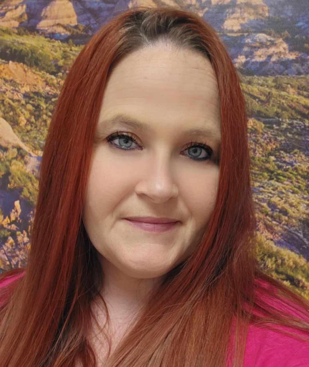 A woman with long red hair and blue eyes is smiling for the camera.