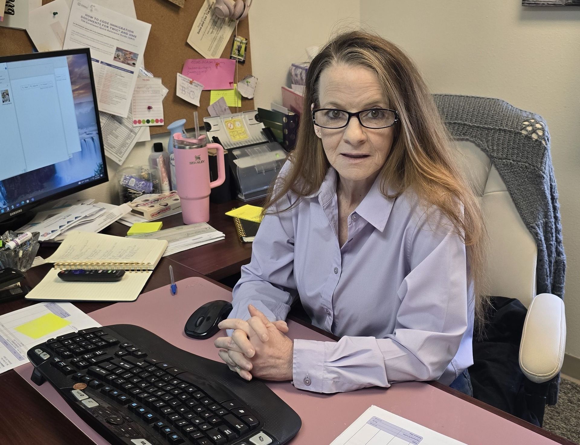 A woman wearing glasses sits at a desk in front of a computer