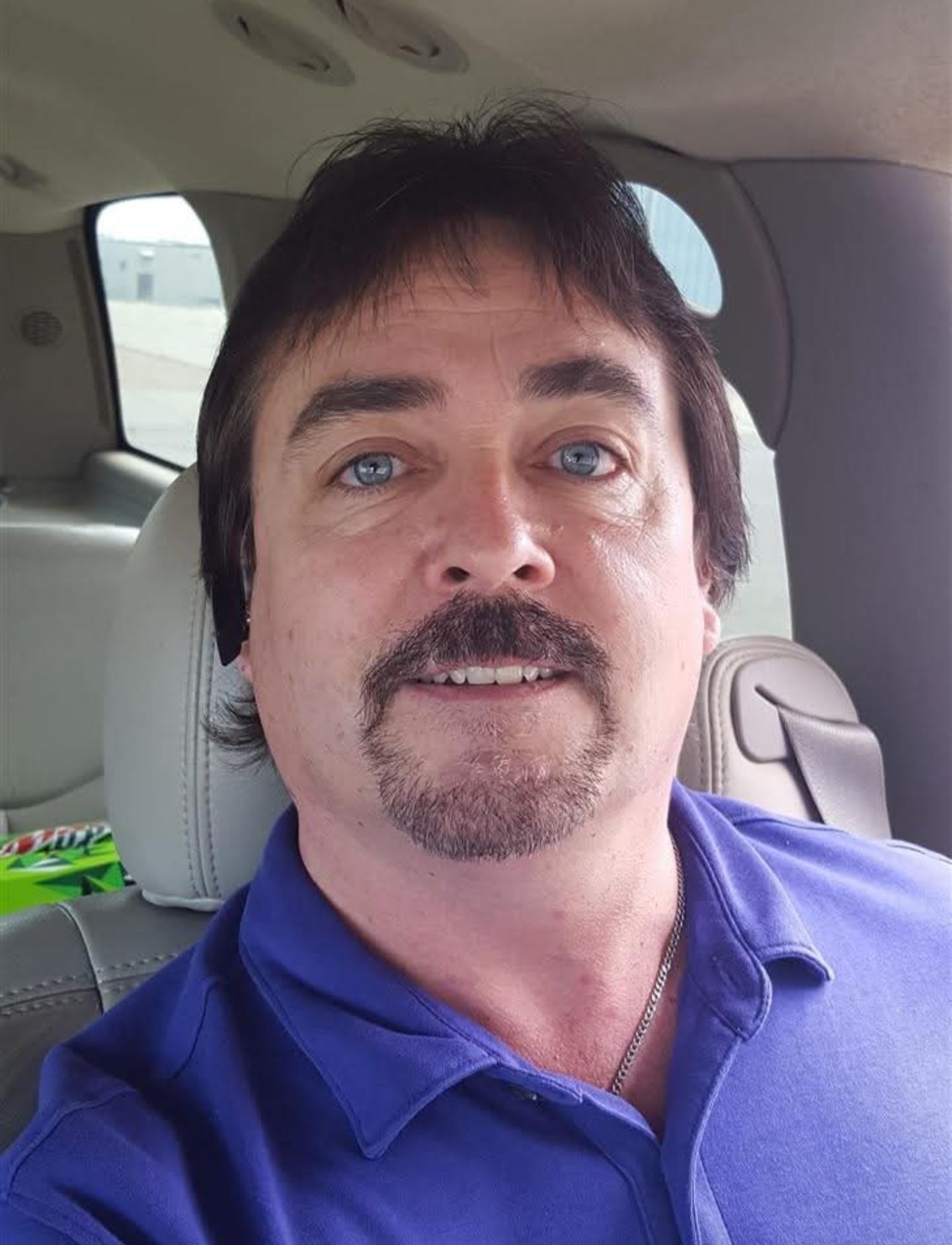 A man with a beard and mustache is sitting in the back seat of a car.