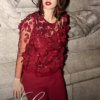 Woman in red top and pants, posing against stone wall.