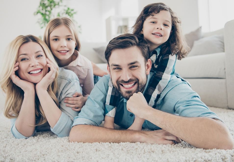 Family of four smiling and lying on a carpet.