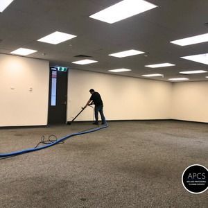 Man cleaning an empty office carpet with a vacuum.