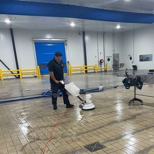 Man cleaning a wet industrial floor with a floor buffer. Blue and white interior.