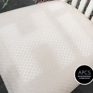 Close-up of a beige chair seat with a diamond pattern, next to a white picket fence.