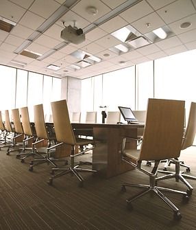Conference room with long table, beige chairs, laptop, projector, and large windows.