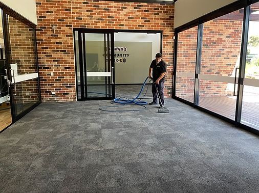 Man cleaning gray carpet in a room with brick walls and glass doors.