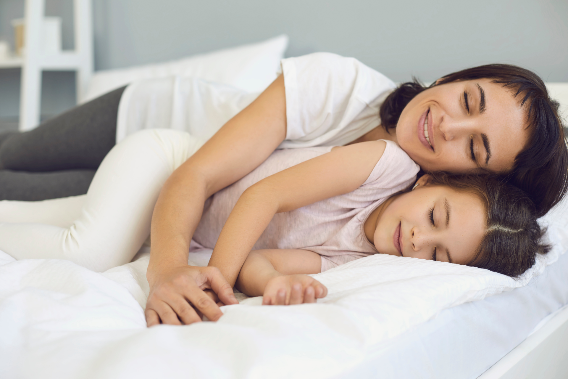 A mother and child, both smiling, lying on a bed together.
