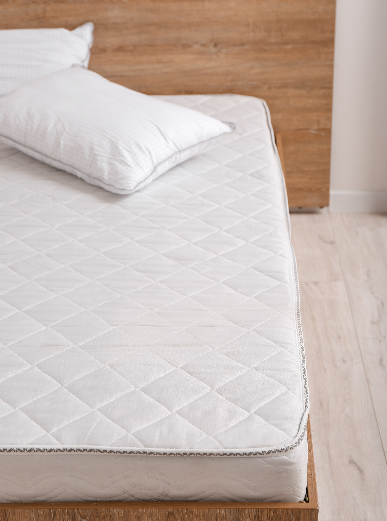 White quilted mattress with pillow on a wooden bed frame.