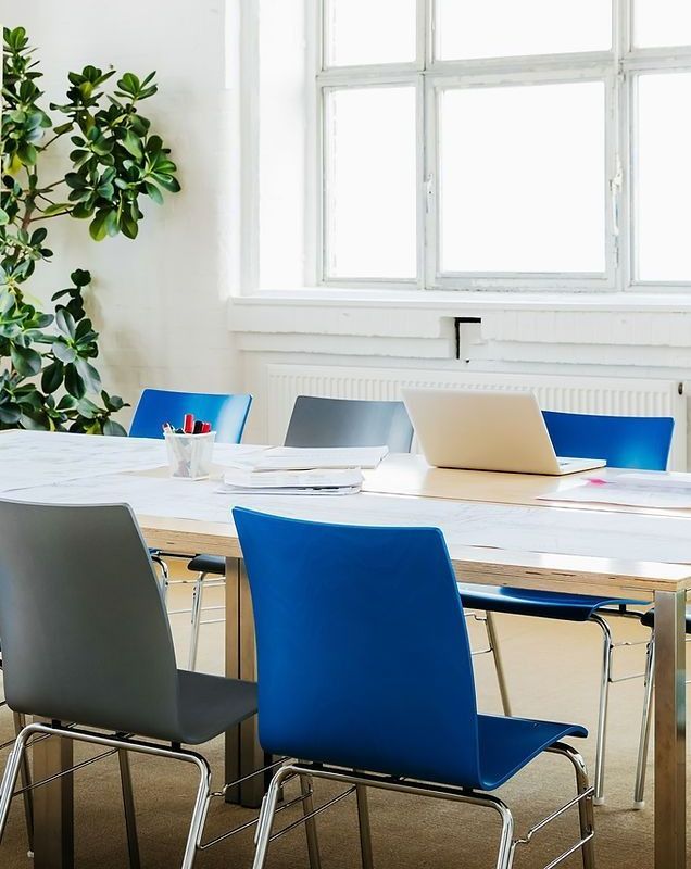 Conference room with a long wooden table, blue and gray chairs, and a laptop.