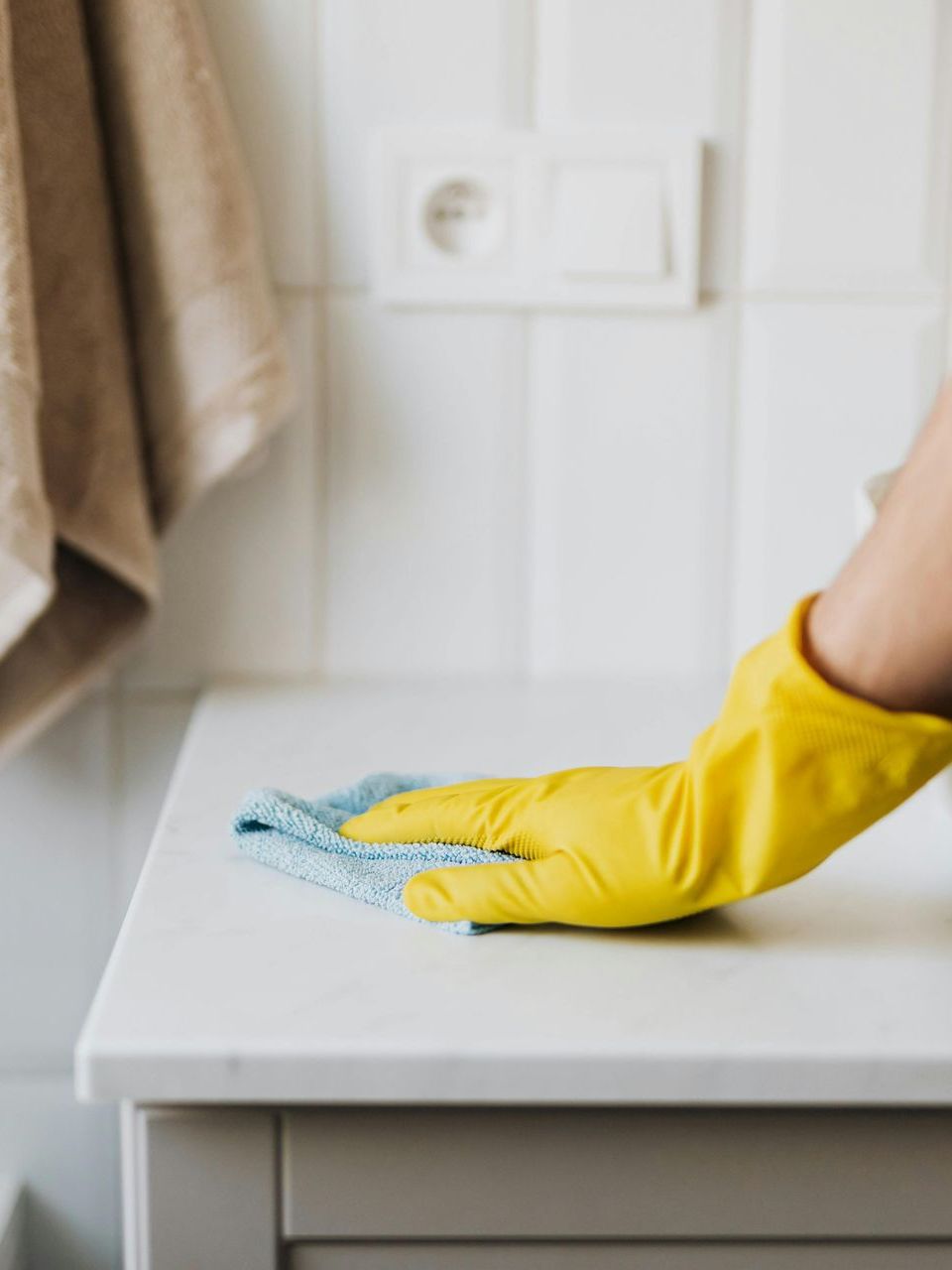 A gloved hand wipes a white surface with a blue cloth in a bathroom for a end of lease clean.