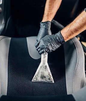 Person in black gloves using a vacuum to clean a car seat.