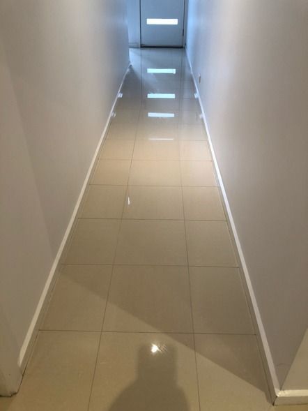 Narrow hallway with tile floor, white walls, and overhead lighting.