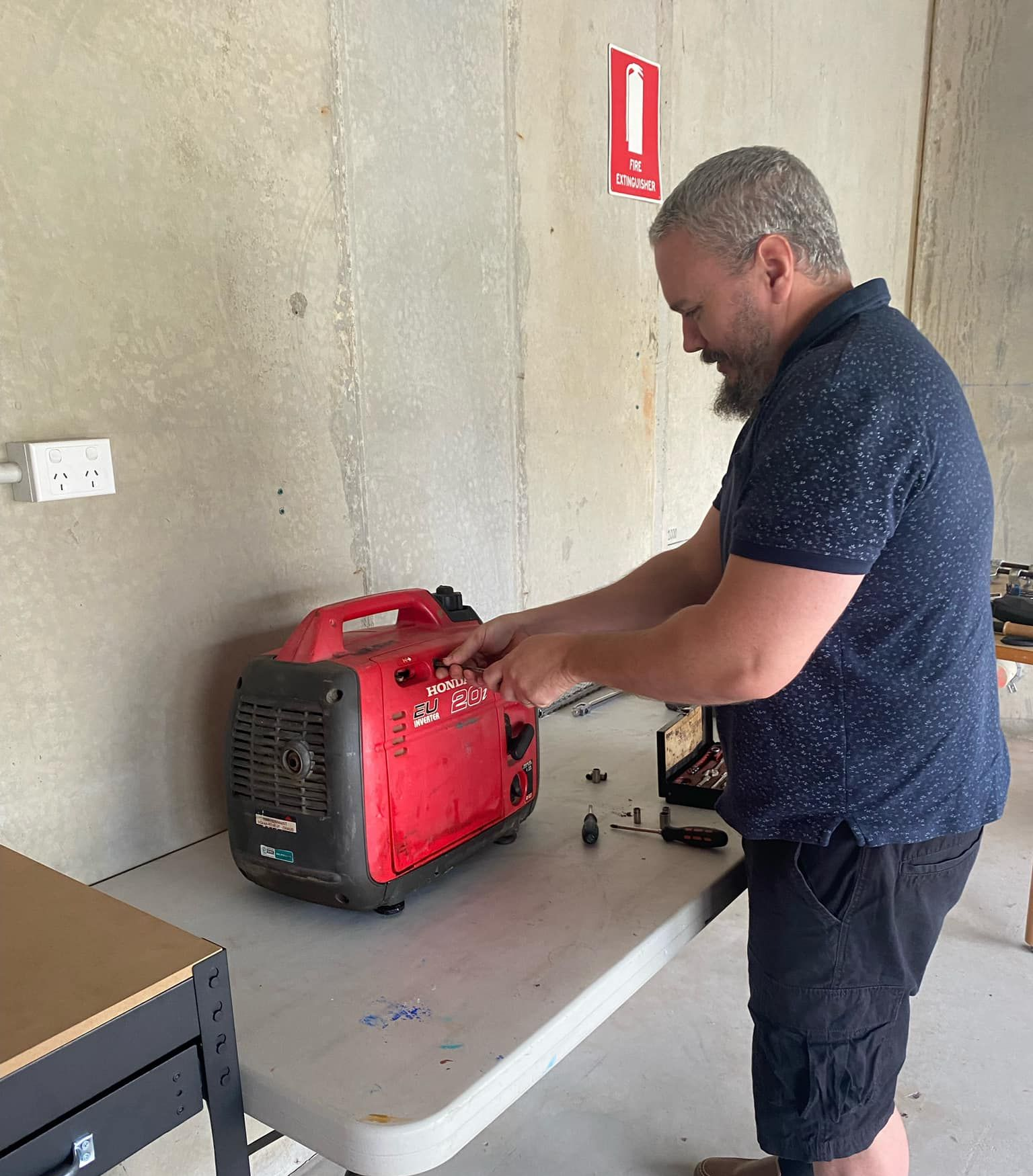 Man Adjusting a Red Generator on a Table Indoors Near a Wall — Cairns Small Engine Repairs in Bentley Park, QLD