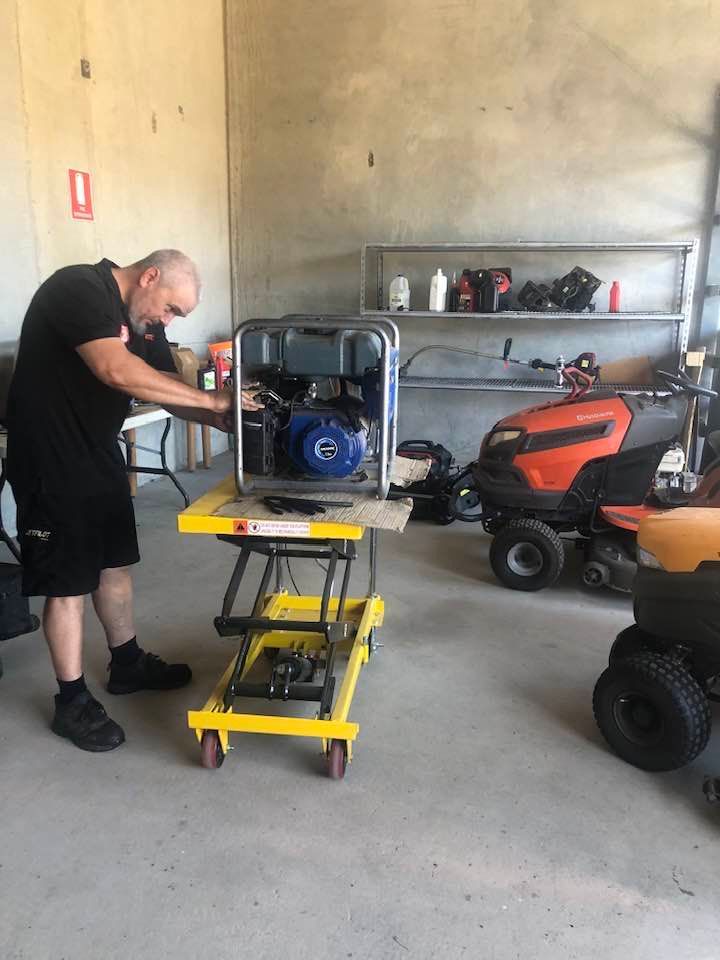 Man Repairs a Lawnmower Engine With a Screwdriver; Outdoors on Grass — Cairns Small Engine Repairs in Bentley Park, QLD