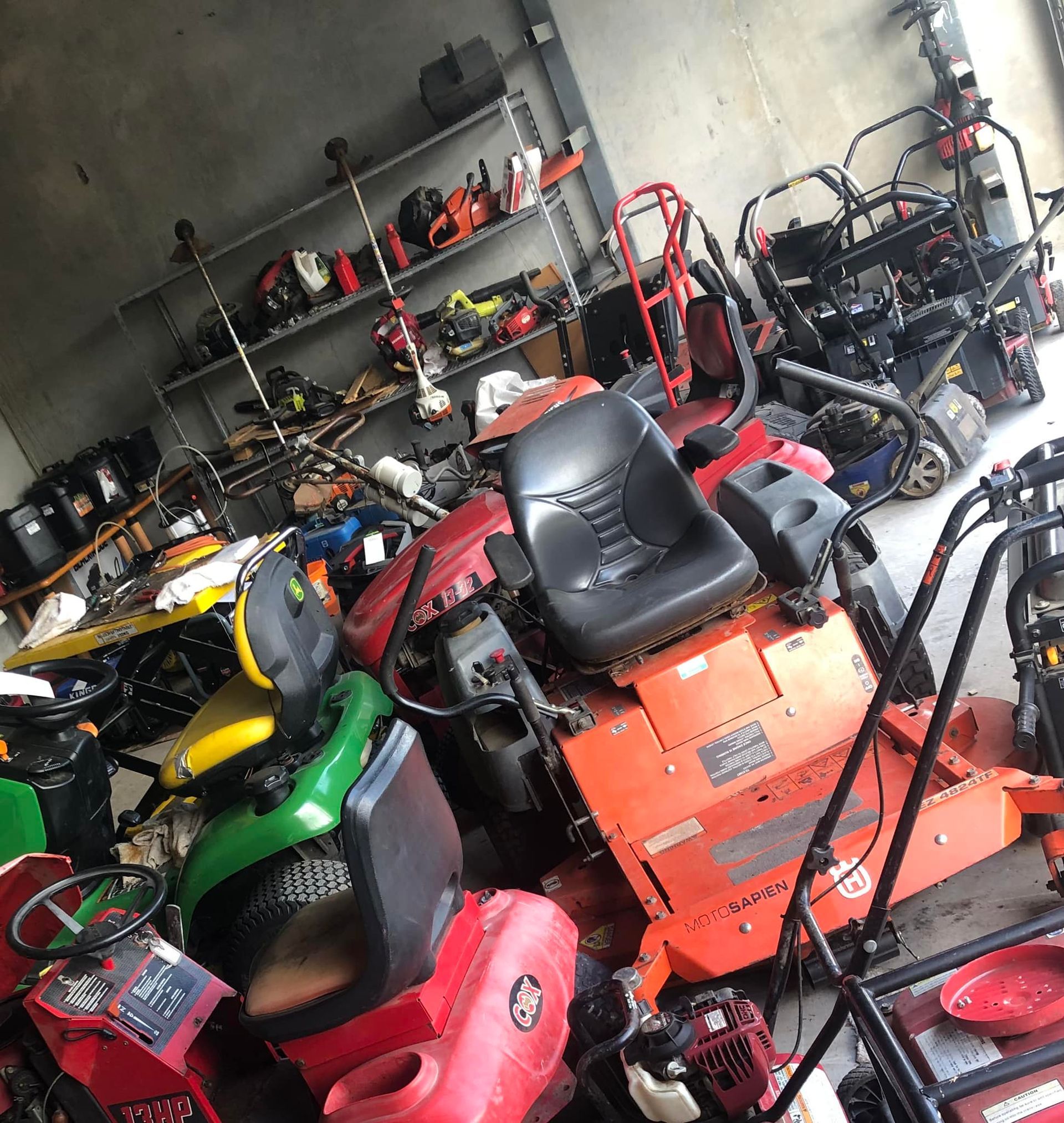 Cluttered garage packed with lawn mowers, go-karts, and tools on shelves — Cairns Small Engine Repairs in Bentley Park, QLD