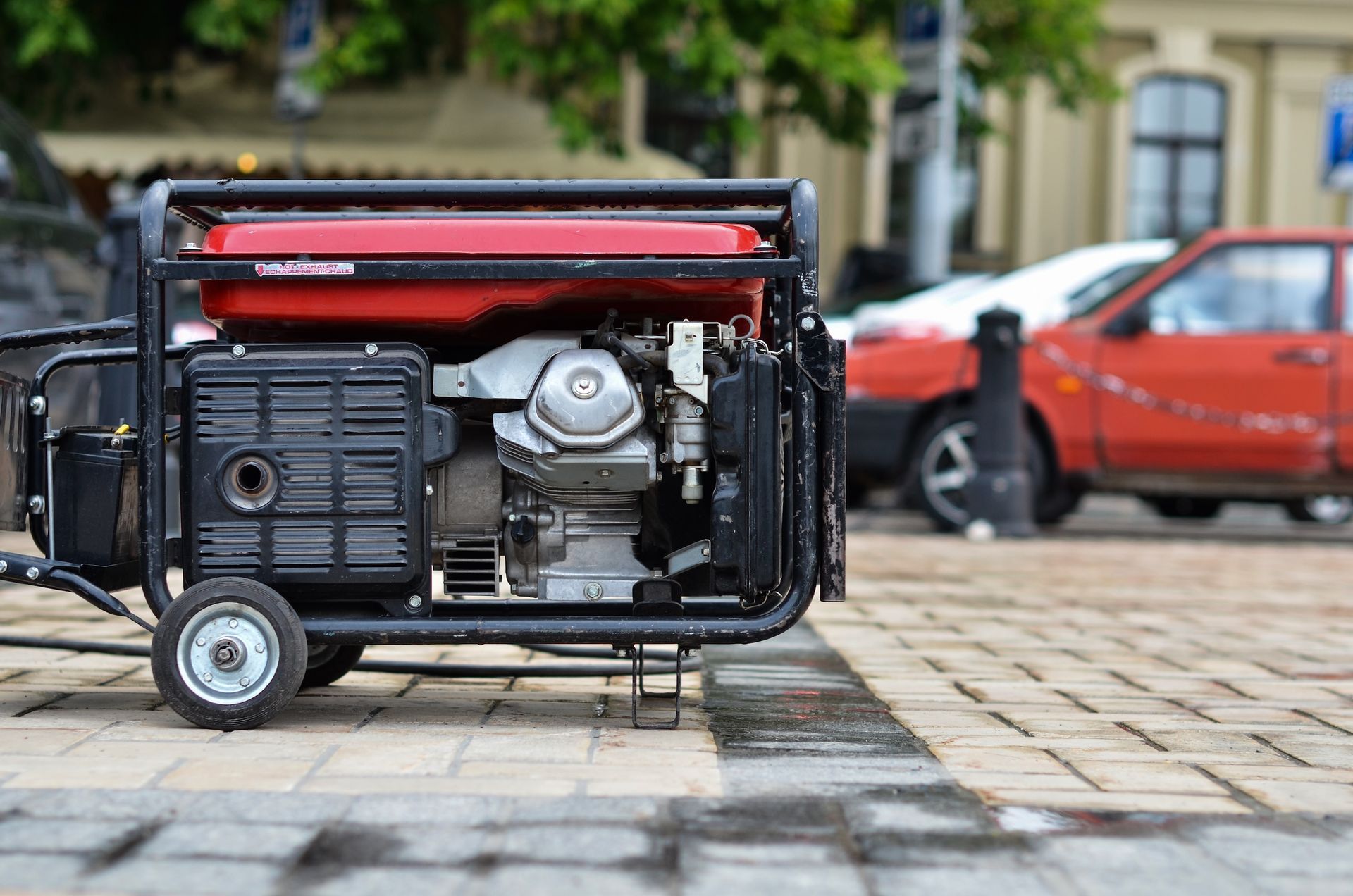 Red and Black Portable Generator on a Brick Sidewalk Next to Parked Cars — Cairns Small Engine Repairs in Bentley Park, QLD