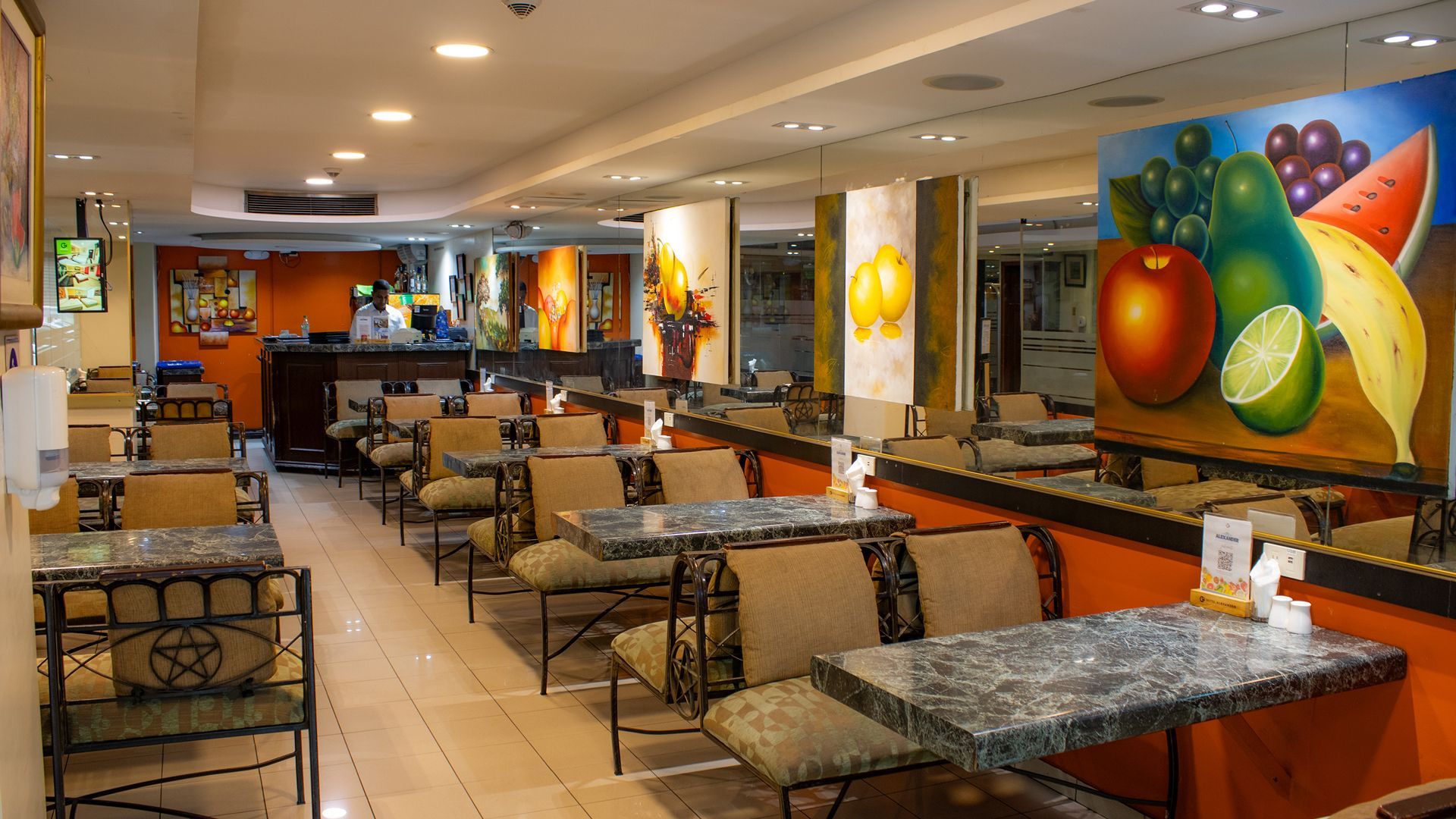Un restaurante con mesas y sillas, y una pintura de frutas en la pared