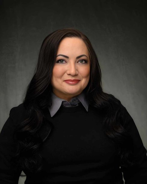 Studio portrait of a woman in a black sweater and gray collared shirt against a dark background