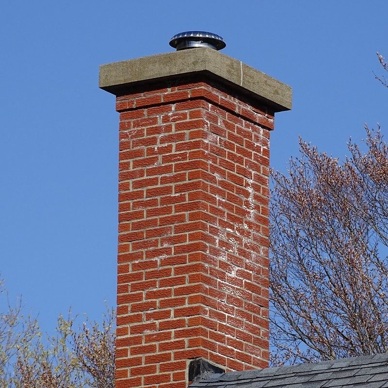 A brick chimney is sitting on top of a roof with trees in the background