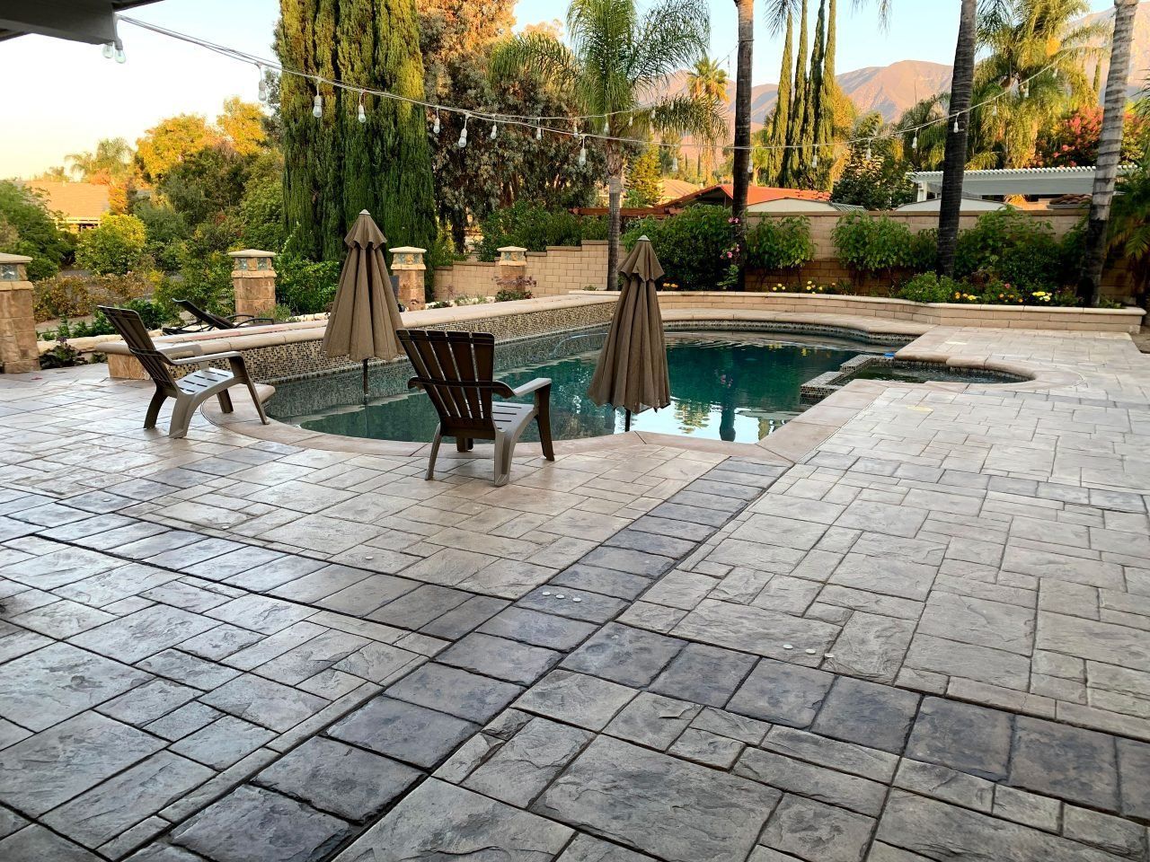 A patio with chairs and umbrellas next to a swimming pool.