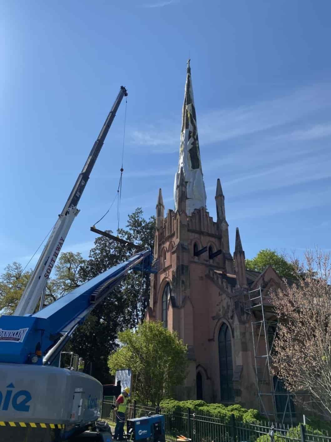 A crane is working on the steeple of a church.