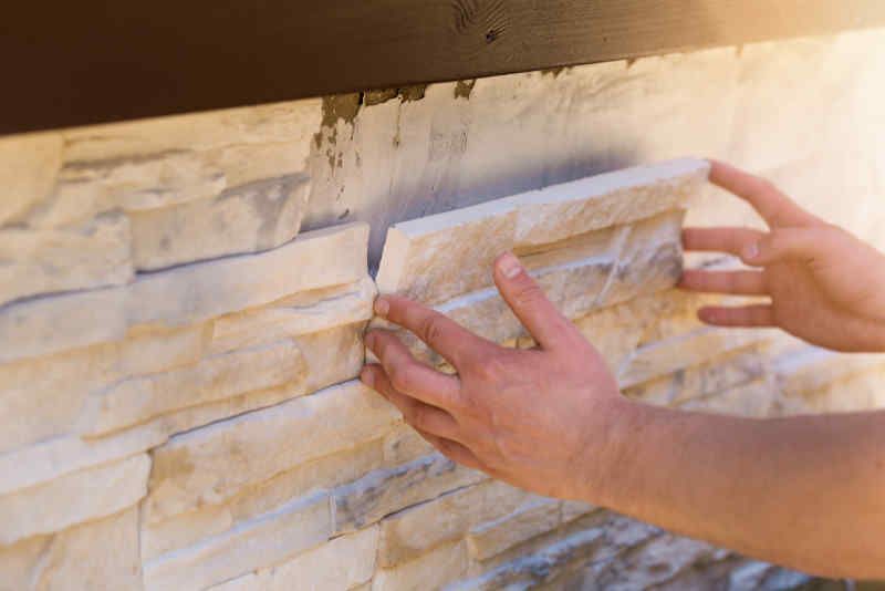 A person is installing a stone wall tile on a wall.