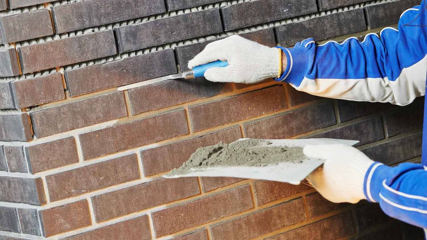 A man is applying mortar to a brick wall with a trowel.