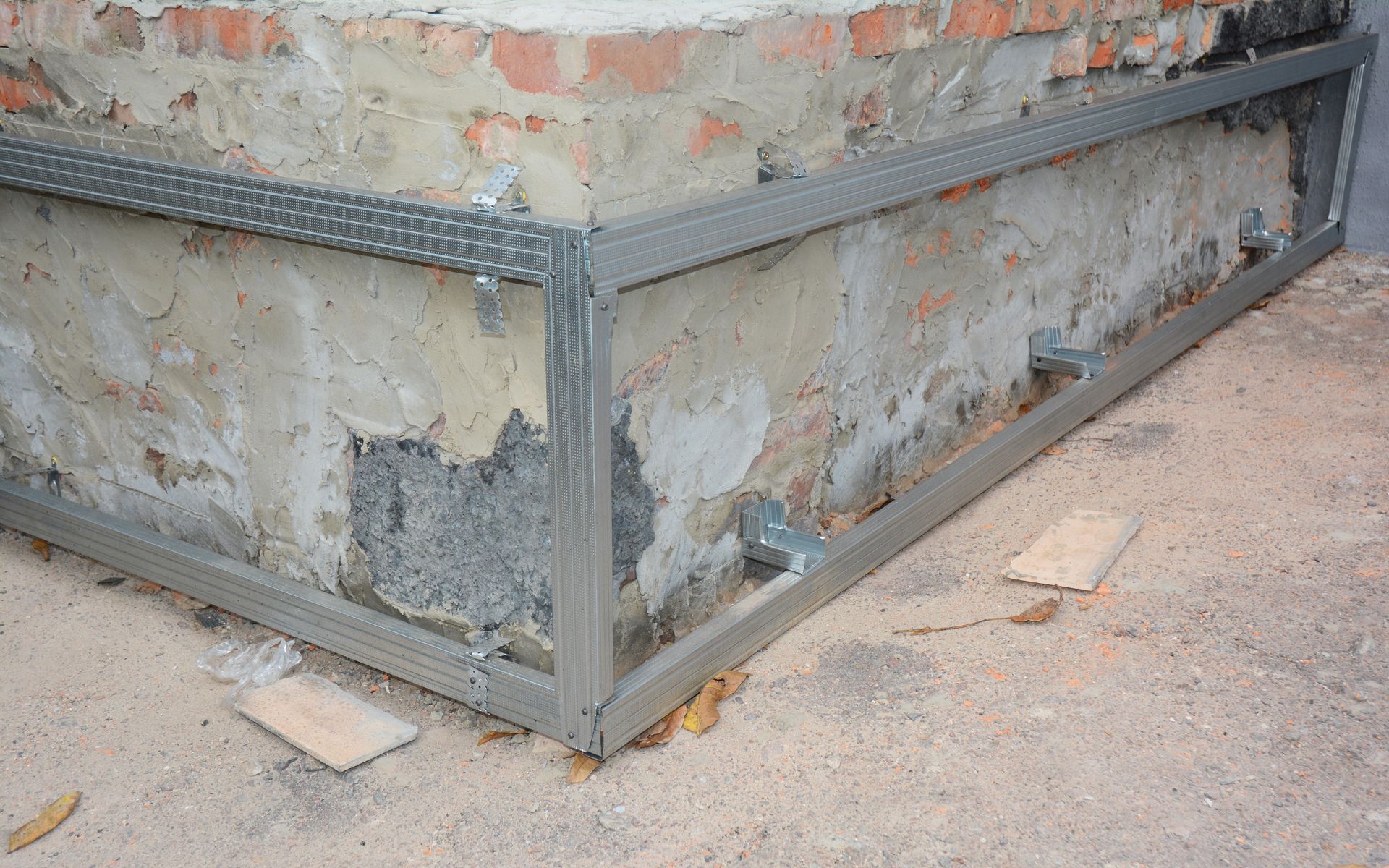 A metal frame is sitting on the ground next to a brick wall.