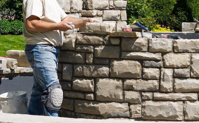 A man is laying bricks on a stone wall.
