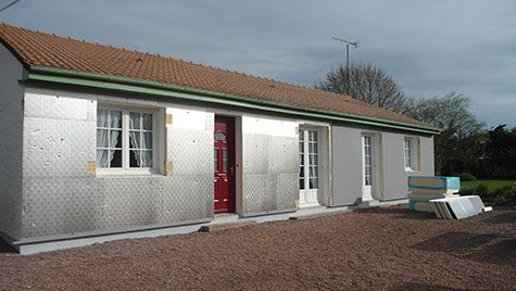 Une maison argentée avec une porte rouge et un toit vert