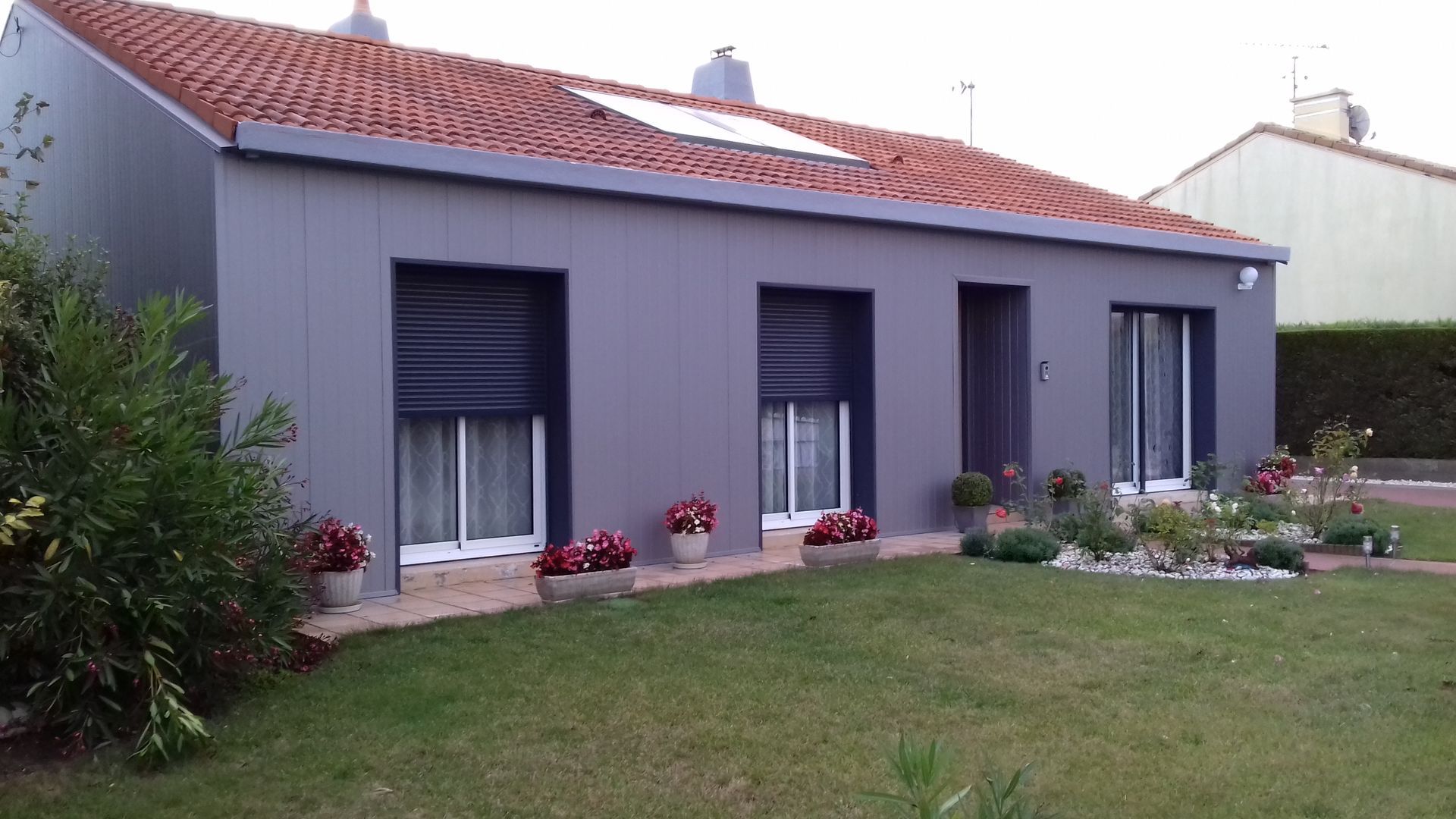 Une maison grise avec un toit de tuiles rouges et une pelouse devant