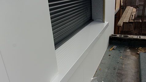 Un mur blanc avec une fenêtre et un volet dessus.