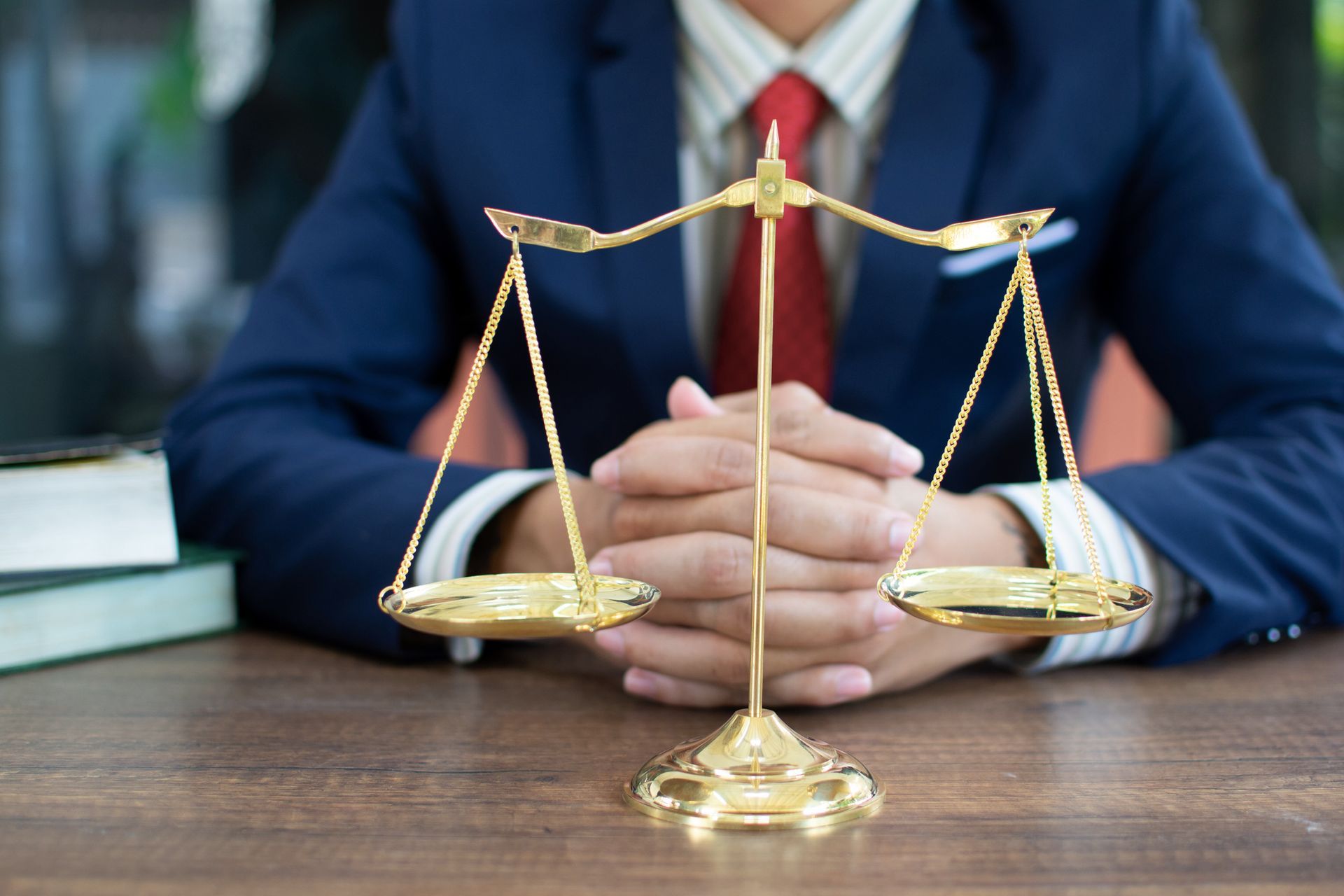 Person in suit with gold scales on a desk, symbolizing justice, with books nearby.