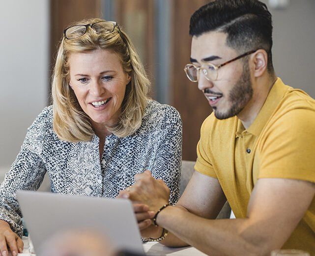 Woman and man looking at a laptop, both smiling. They are indoors at a table.