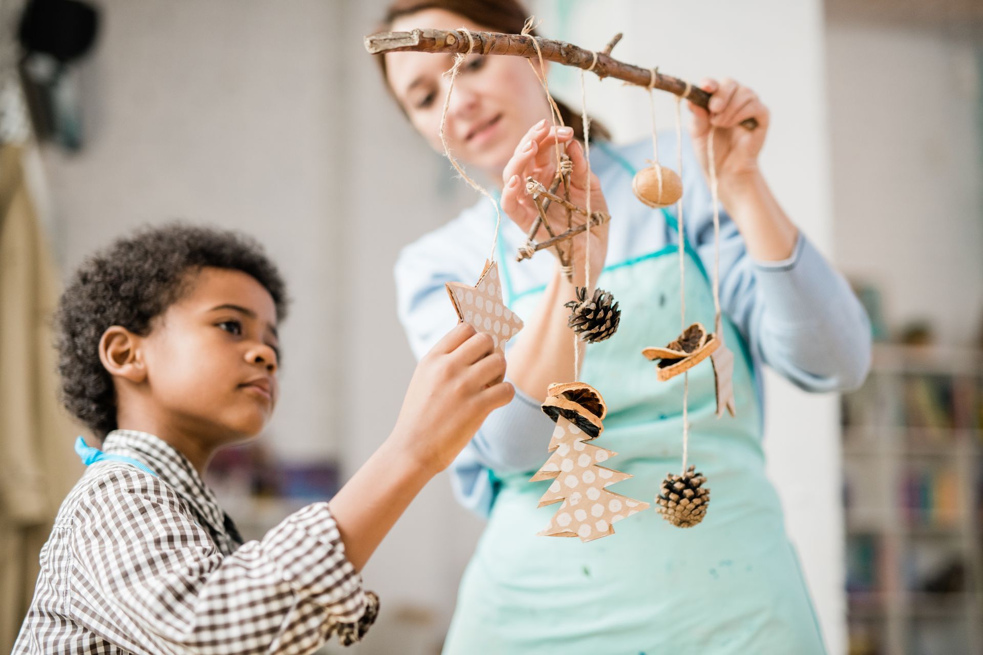 A person and a child craft a mobile with wooden shapes and natural elements in a bright room.