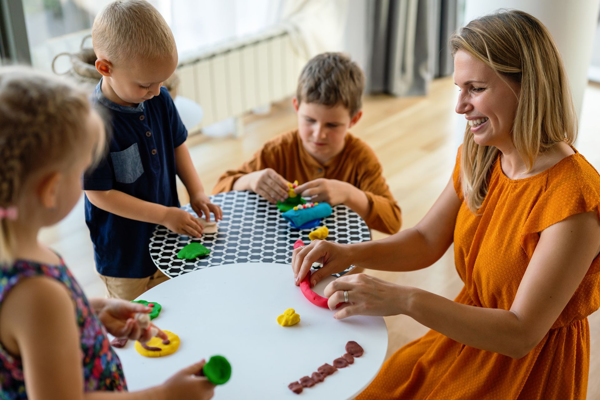 Woman and three children playing with colorful modeling clay at a round table.