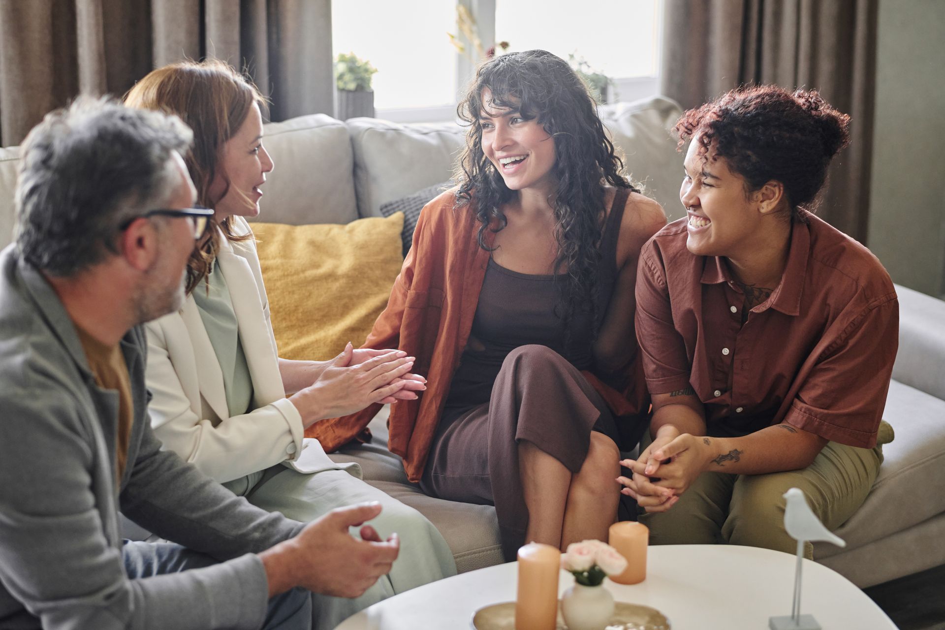 Group of people sitting on a couch, smiling and talking. Indoors, neutral tones.