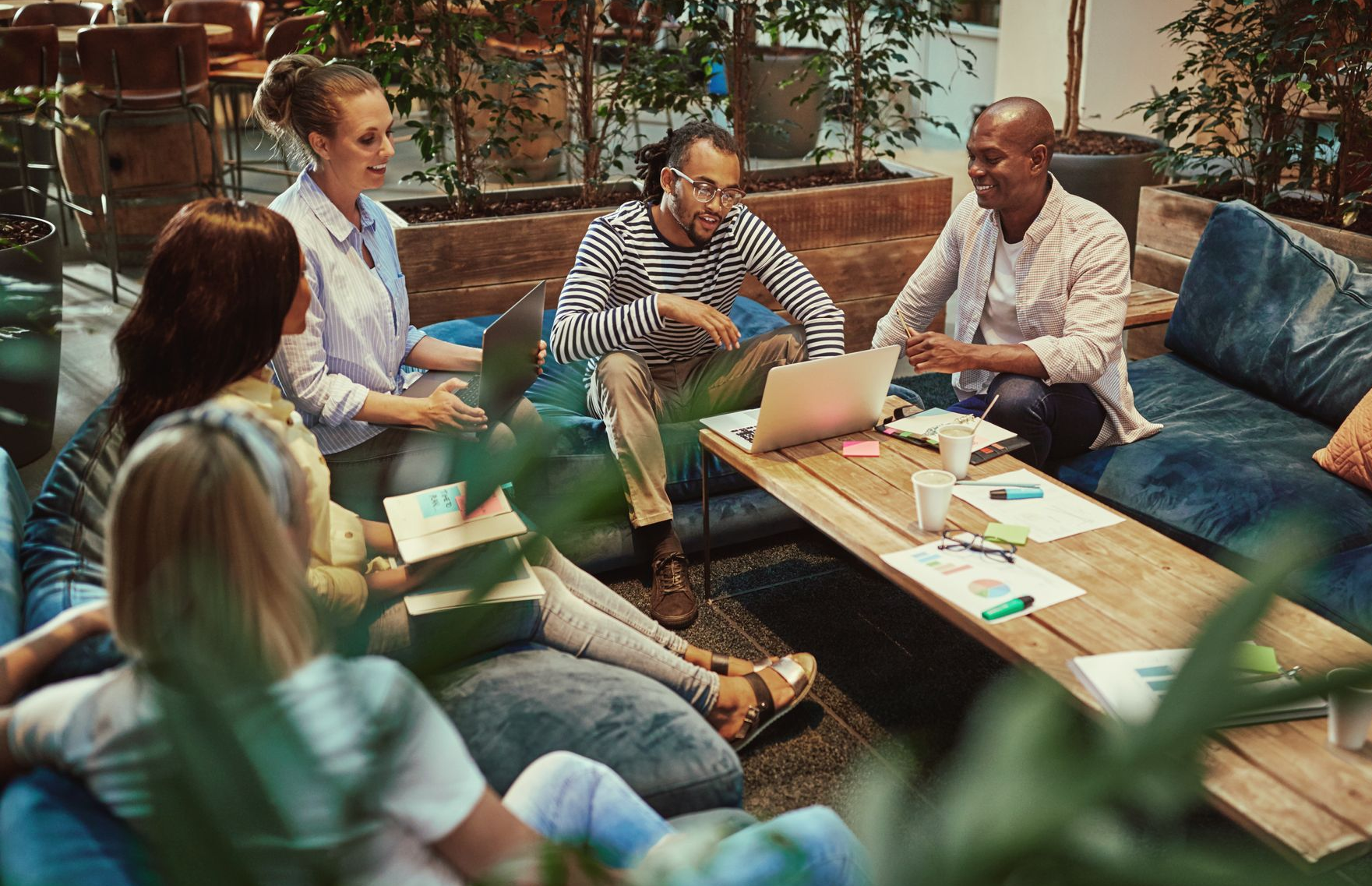 Group of people in casual setting, discussing, looking at a laptop and papers on a coffee table.