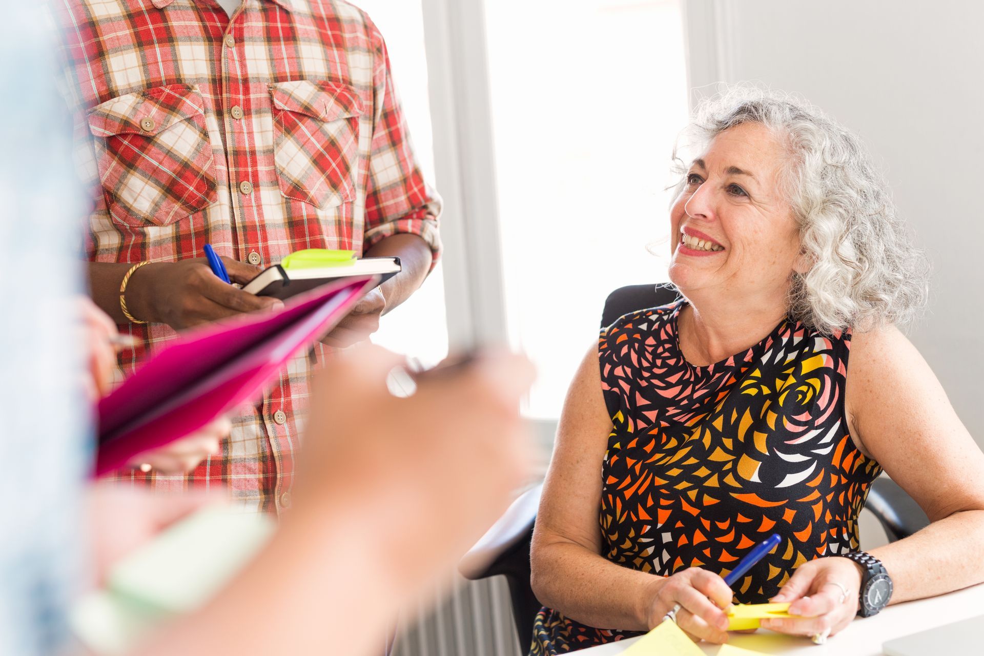 Group of people in an office. A woman smiles while others hold sticky notes.