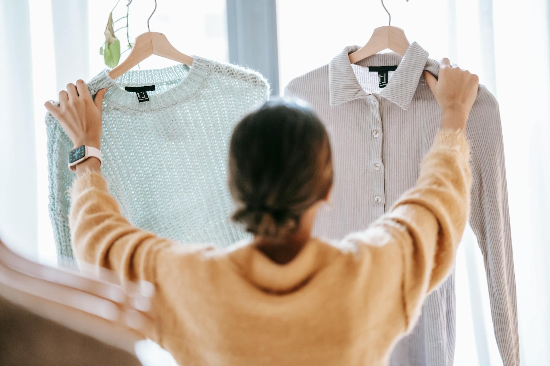 A woman is holding a sweater and a shirt on a hanger.