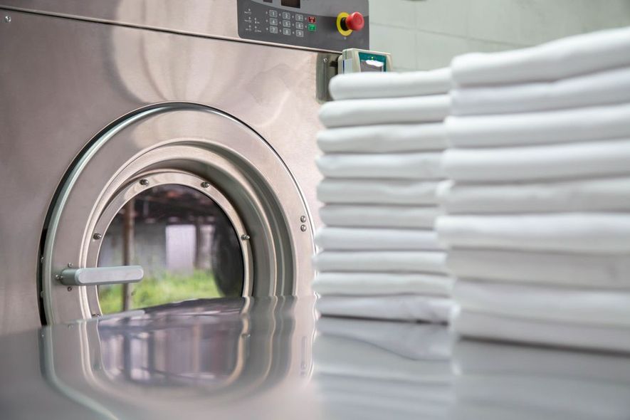 A stack of towels is sitting next to a washing machine in a laundromat.