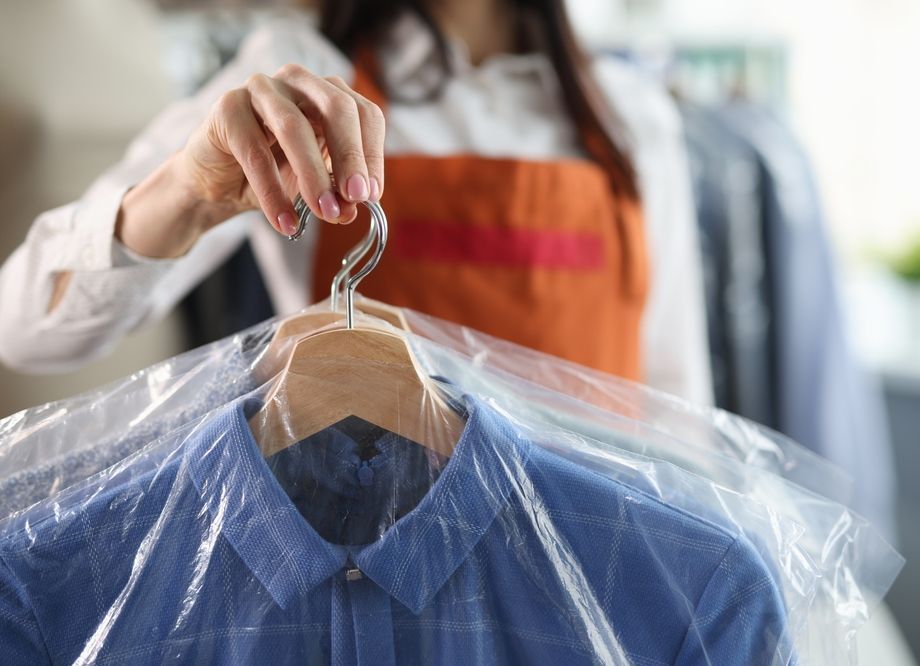 A woman is hanging a shirt wrapped in plastic on a hanger.