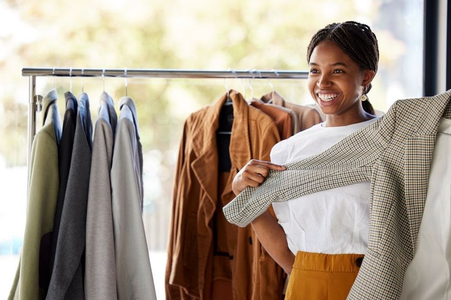 A woman is holding a sweater in front of a rack of clothes.