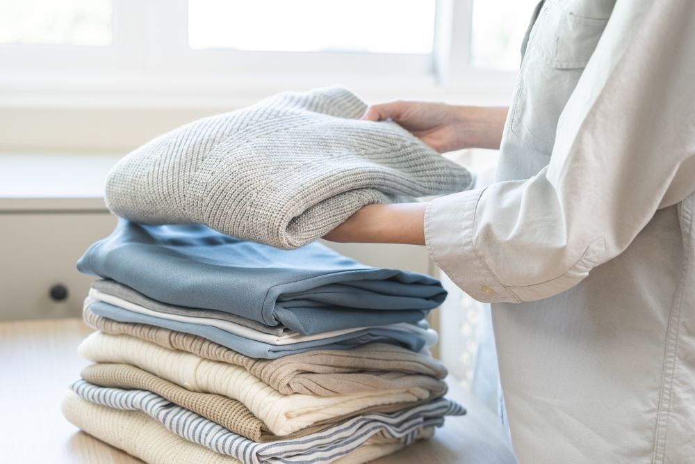 A person is holding a stack of clothes on a table.