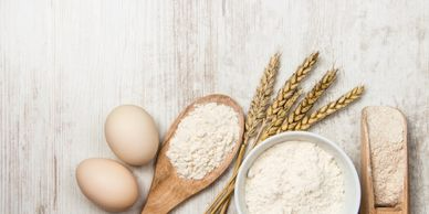 A bowl of flour , eggs , and wheat ears on a wooden table.