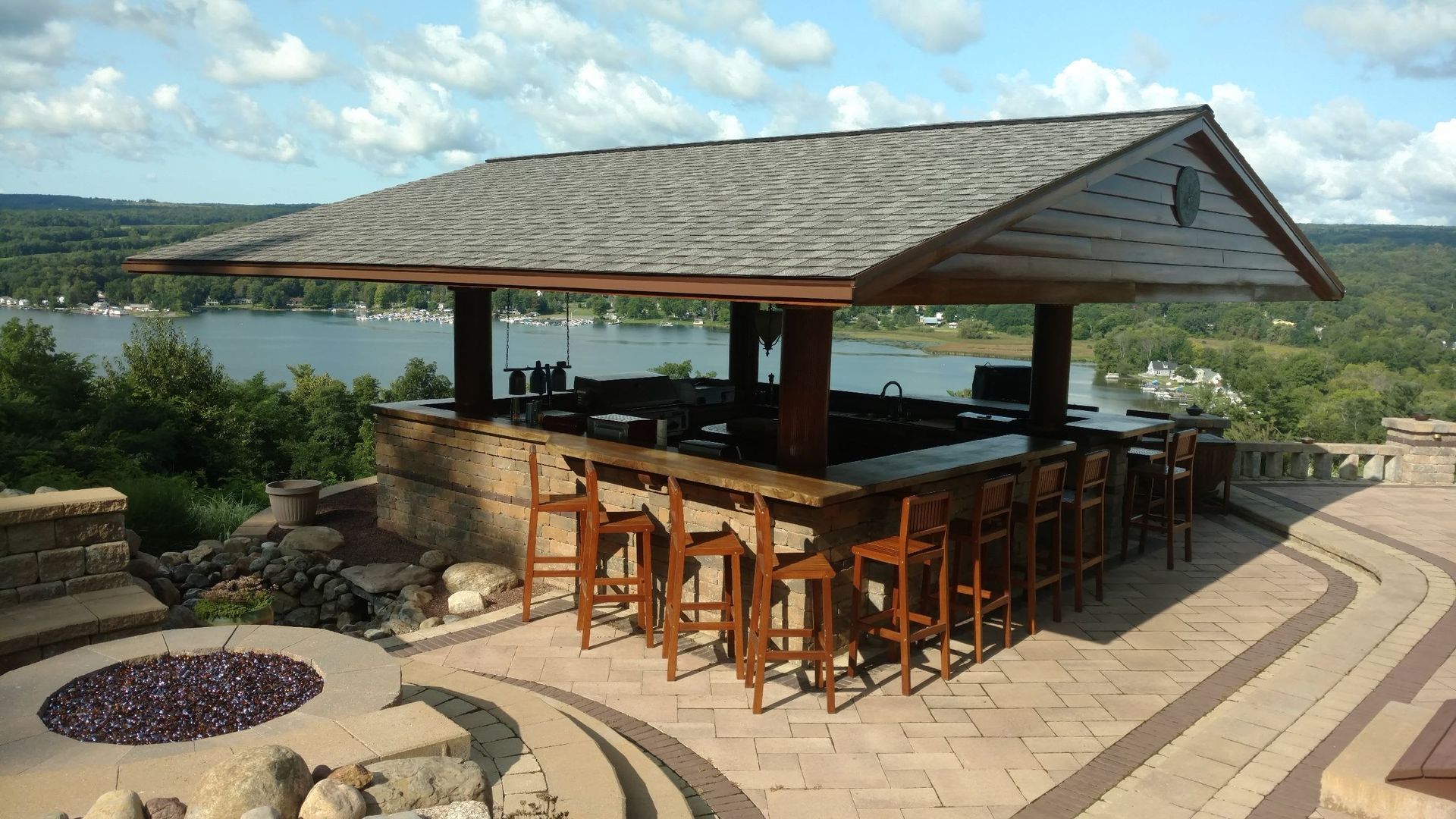 A gazebo with a bar and stools on a patio overlooking a lake