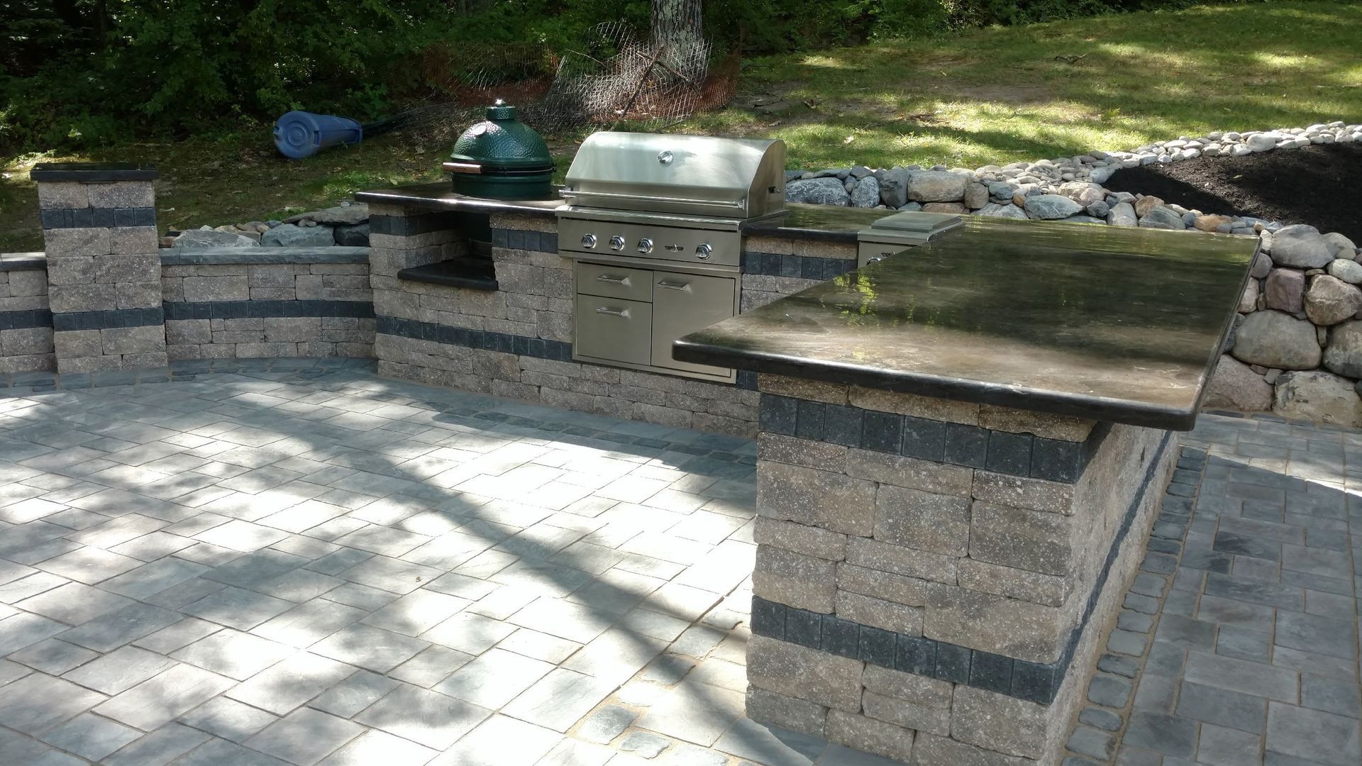 A grill is sitting on top of a brick patio next to a stone wall