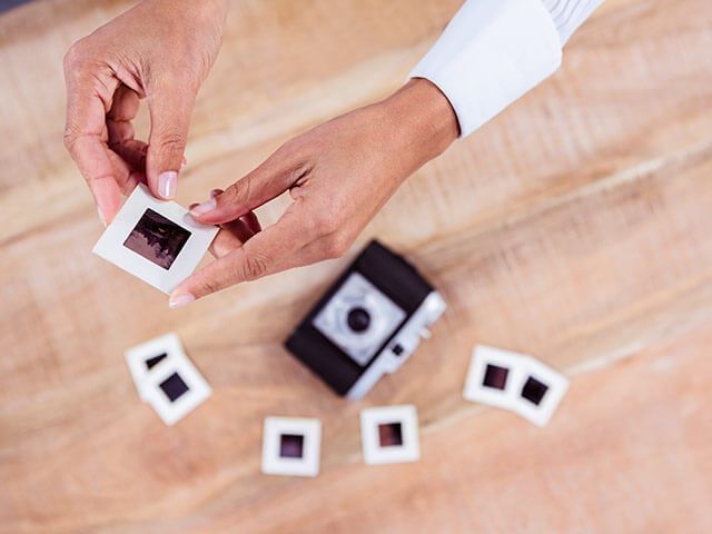 A person is holding a slide next to a camera on a wooden table.