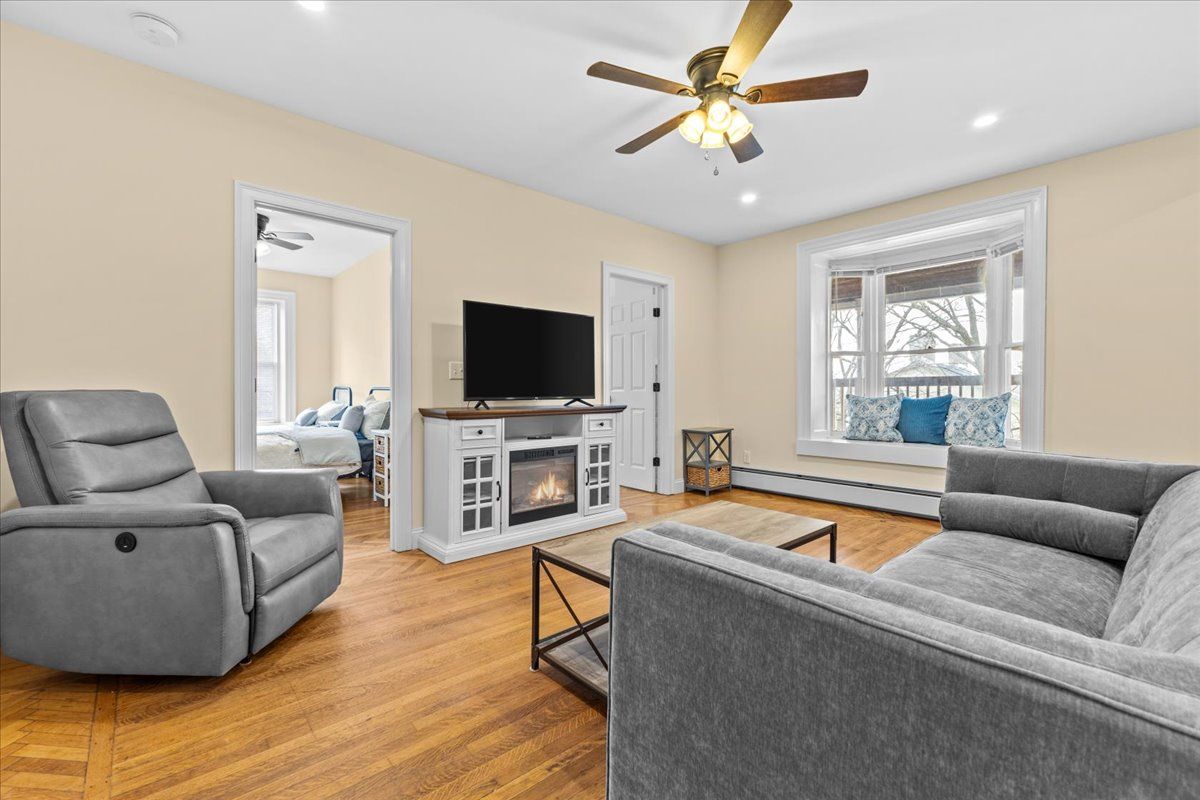 Living room with gray furniture, fireplace, ceiling fan, and window seat.
