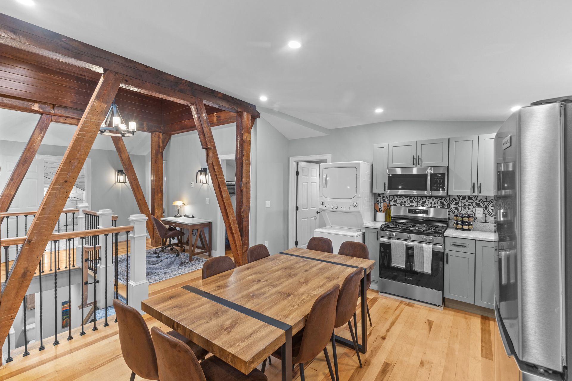 Kitchen with dining area, hardwood floors, exposed wooden beams, stainless steel appliances, and a table set for dining.
